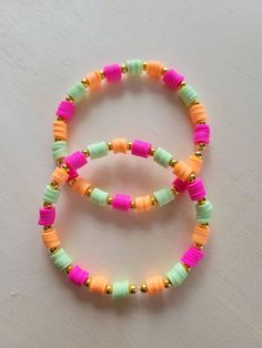 two bracelets with different colored beads on a white surface, one is yellow and the other is pink