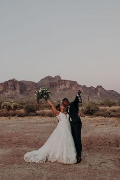 a bride and groom standing in the desert with their arms up to each other holding flowers