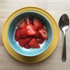 strawberries are in a bowl with yogurt and a spoon next to it