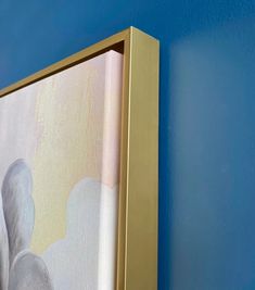 a painting hanging on the side of a blue wall with a gold frame and white clouds painted on it