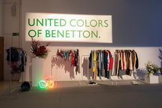 the interior of a clothing store with clothes on racks and neon lights in front of it