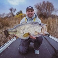 a man holding a large fish while sitting on top of a boat in the water