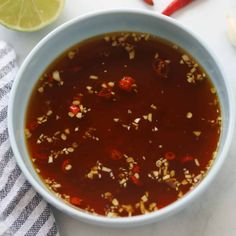 a white bowl filled with soup next to sliced red peppers and limes on a table