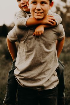 two young boys hugging each other in the middle of a field