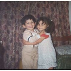 two young children hugging each other in front of a curtain