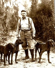 a man standing next to four dogs on a dirt road