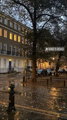 a city street at night with cars parked on the side walk and trees in the rain