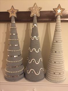 three knitted christmas trees sitting on top of a mantle next to a wooden star