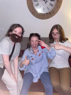 three people sitting on a couch with a clock in the background and one person making a silly face