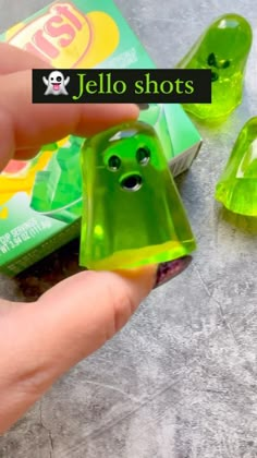 a hand is holding a green candy with eyes and mouth on it, next to two gummy candies