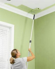 a woman is painting the ceiling with green paint and a mop in her hand