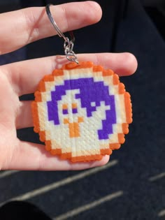 a hand holding a pixel keychain with an orange and purple bird on it