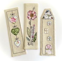 two hand embroidered bookmarks with houses and flowers on them, one in the shape of a house