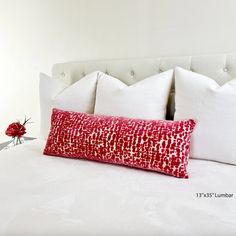 a white bed with red and white pillows on top of it, next to a flower