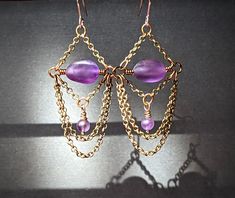 "Smooth matte amethyst pebbles draped with two lengths of brass chain and accented by small round amethyst beads. Surgical steel ear wire. MADE TO ORDER, ships in 3-5 business days. Length:  2.25\" from top of ear wire to bottom of chain Width:  1\"" Purple Amethyst Beaded Chain Jewelry, Purple Metal Dangle Chandelier Earrings, Purple Metal Chandelier Dangle Earrings, Purple Dangle Chandelier Earrings, Gold Amethyst Dangle Chandelier Earrings, Bohemian Amethyst Chandelier Earrings Gift, Purple Wire Wrapped Chandelier Drop Earrings, Purple Amethyst Earrings With Dangling Beads, Handmade Amethyst Chandelier Earrings