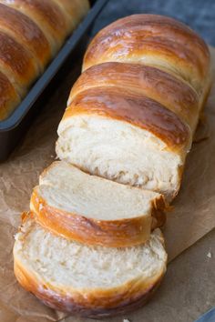 sliced loaf of bread sitting on top of a piece of wax paper next to a baking pan