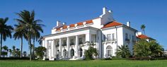 a large white house with red roof and palm trees in the foreground on a sunny day