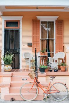 an orange bicycle is parked in front of a pink house with shutters and potted plants