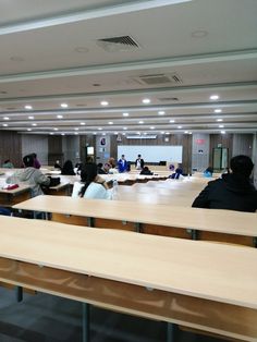 people sitting at desks in a large room with wooden tables and chairs around them