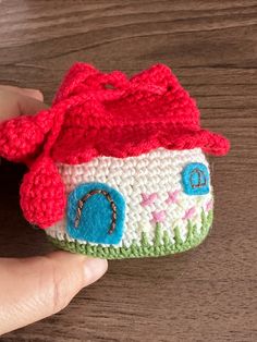 a hand holding a small crocheted doll with a red hat on it's head