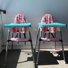 two children's high chairs sitting next to each other in front of a wall