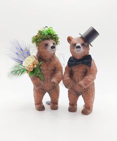 two brown teddy bears wearing hats and bow ties, standing next to each other with flowers on their heads