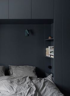 an unmade bed in a dark room with bookshelves and shelves on the wall