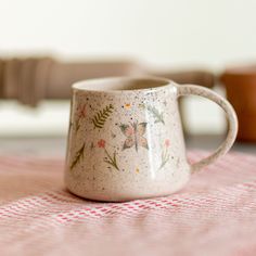 a white coffee mug sitting on top of a red and white checkered table cloth