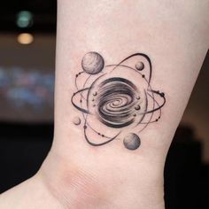 a black and white tattoo on the ankle of a woman with planets around her neck