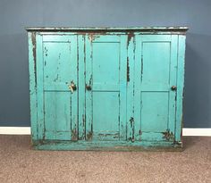 an old blue cabinet with peeling paint on the top and bottom doors, in front of a gray wall