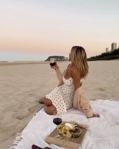 a woman sitting on top of a beach holding a glass of wine