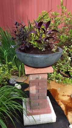 a potted plant sitting on top of a brick pillar in the middle of a garden