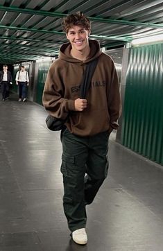 a young man is walking down the street wearing a brown sweatshirt and green cargo pants