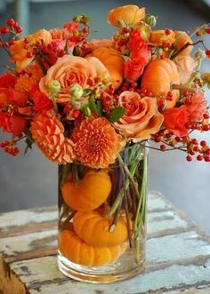 a vase filled with oranges and flowers on top of a table