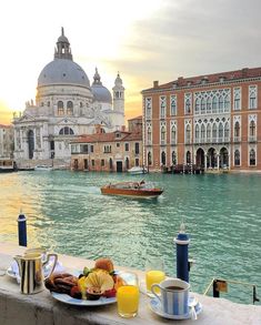 a table with food and drinks on it next to the water in front of buildings