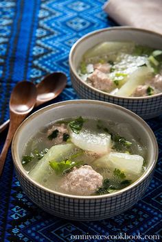 two bowls filled with meat and vegetables on top of a blue table cloth next to spoons