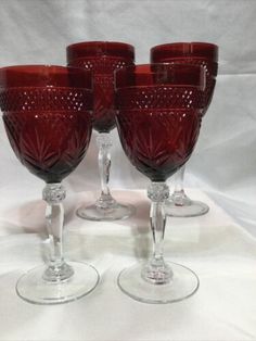 four red wine glasses sitting on top of a white table covered in lace and cloth