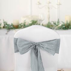 the back of a white chair with a gray bow on it and candles in the background