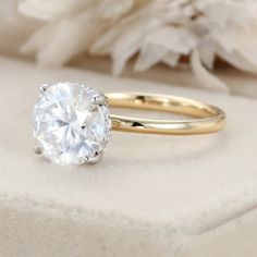 a close up view of a diamond ring on a white cloth with flowers in the background