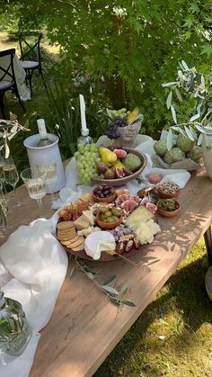 a wooden table topped with plates and bowls filled with food on top of grass covered ground