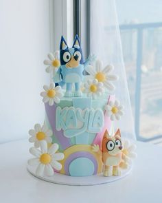 a cake decorated with cartoon characters and daisies on a window sill in front of a window