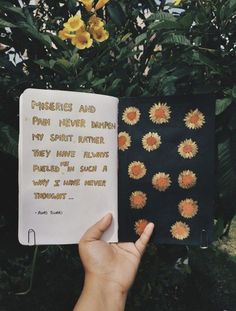 someone is holding up a book that has flowers on it and the pages are written in gold