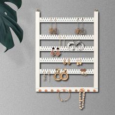 a white wall mounted jewelry rack with earrings and bracelets hanging from it's sides