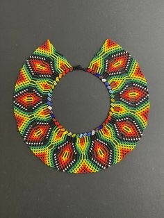 "This Trendy Multicolor Oversized Necklace was made using ancestral beading techniques by the Embera Chami tribe of Colombia. Their pieces are all handmade, and the designs and colors used are unique to their tribe and related to their everyday lives.   This stunning one-of-a-kind Retro Necklace would surely make your outfit pop and is the perfect eye-catching piece needed to complete your look.  Colors: Greens, Black, Reds, Yellows, Orange, and Blues  Length:16\" Width: 3\" Check out other simi Traditional Fair Trade Beaded Necklaces For Festivals, Traditional Handmade Bib Necklace With Round Beads, Artisan Beaded Necklaces With Round Beads For Festivals, Traditional Fair Trade Beaded Necklaces With Round Beads, Traditional Colorful Beads Bib Necklace, Multicolor Traditional Bib Necklace With Large Beads, Traditional Large Beads Bib Necklaces For Festivals, Handwoven Multicolor Beaded Necklaces, Multicolor Bohemian Beaded Bracelets Fair Trade