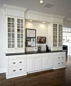 a kitchen with white cabinets and black counter tops, along with wooden floors in front of it