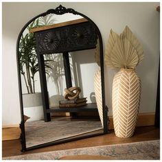 a mirror sitting on top of a wooden floor next to a vase