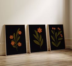 three framed art pieces with orange flowers on black and brown background, sitting in front of a white wall