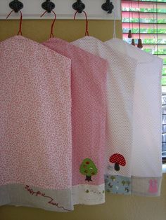 three pink towels hanging from hooks on a wall next to a window with blind shades