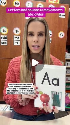 a woman sitting at a desk holding up a sign with letters and sounds on it