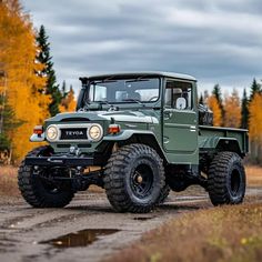 an army green truck parked on the side of a dirt road in front of trees